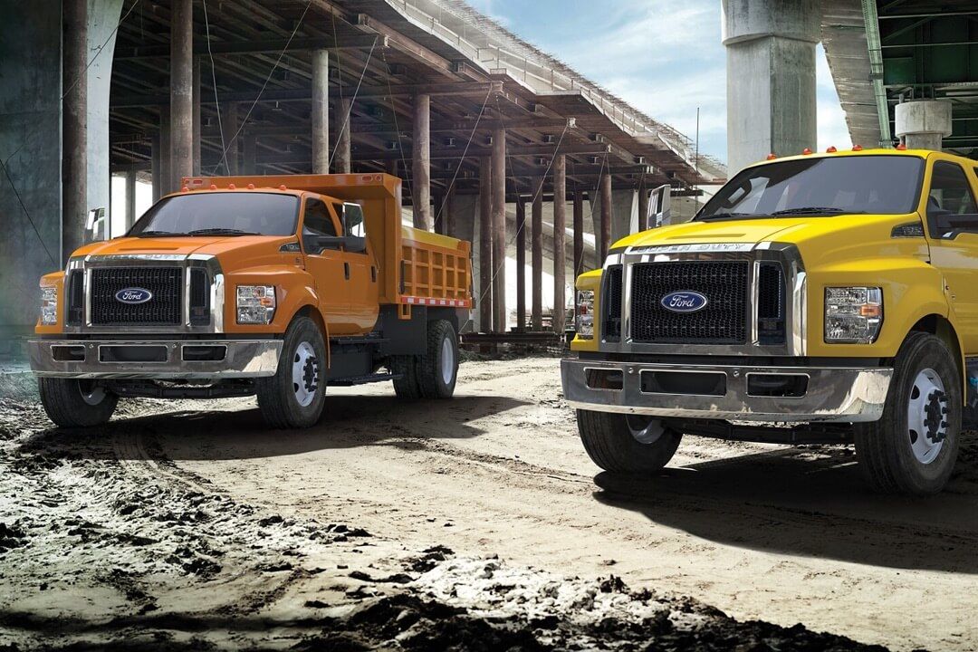 Deux camions commerciaux Ford F-650 et F-750 garés sur une terre bouetteuse.