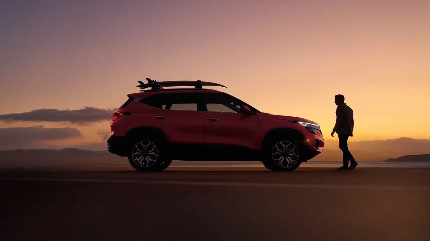 A man stands next to the Kia Seltos at sunset.