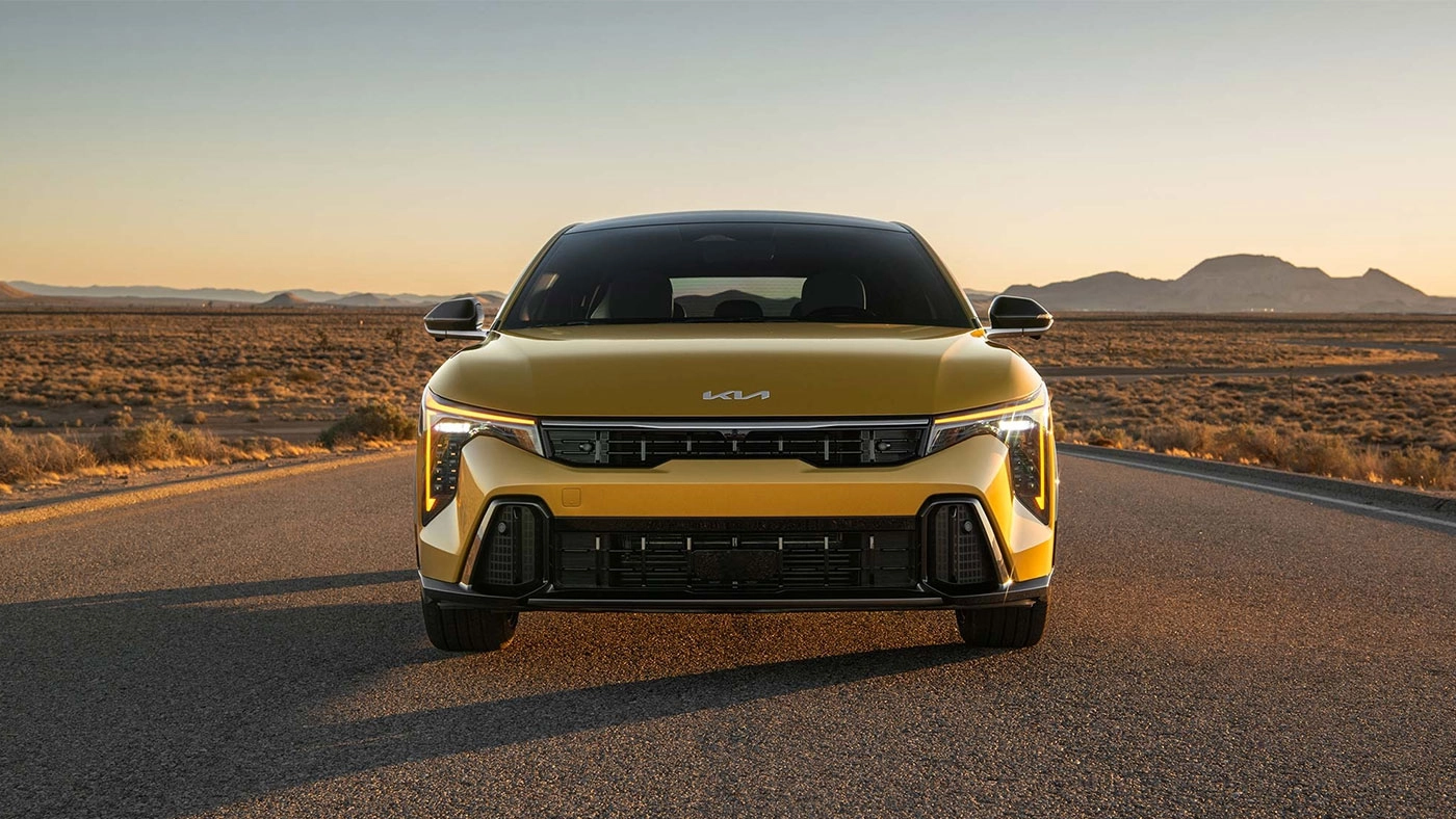 Vue 3/4 avant et lat&eacute;rale du Kia K4 &agrave; hayon 2026 en arr&ecirc;t sur route avec coucher de soleil