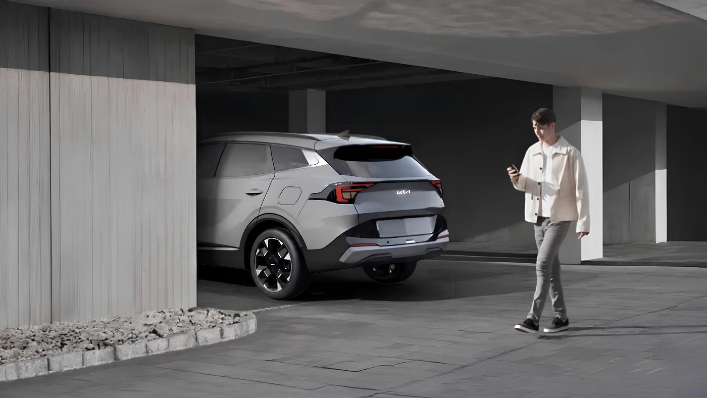 Kia Sportage 2026 gris stationn&eacute; sous un abri, avec une personne tenant un t&eacute;l&eacute;phone &agrave; proximit&eacute;.