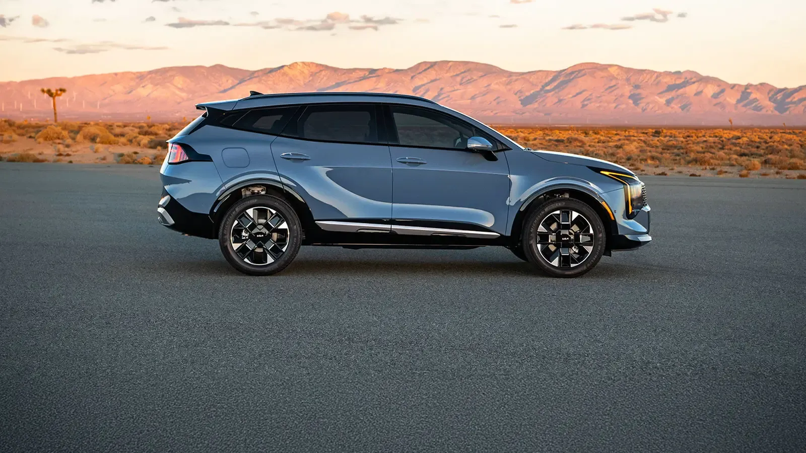 Kia Sportage hybride rechargeable bleu vu de profil dans un paysage montagneux.