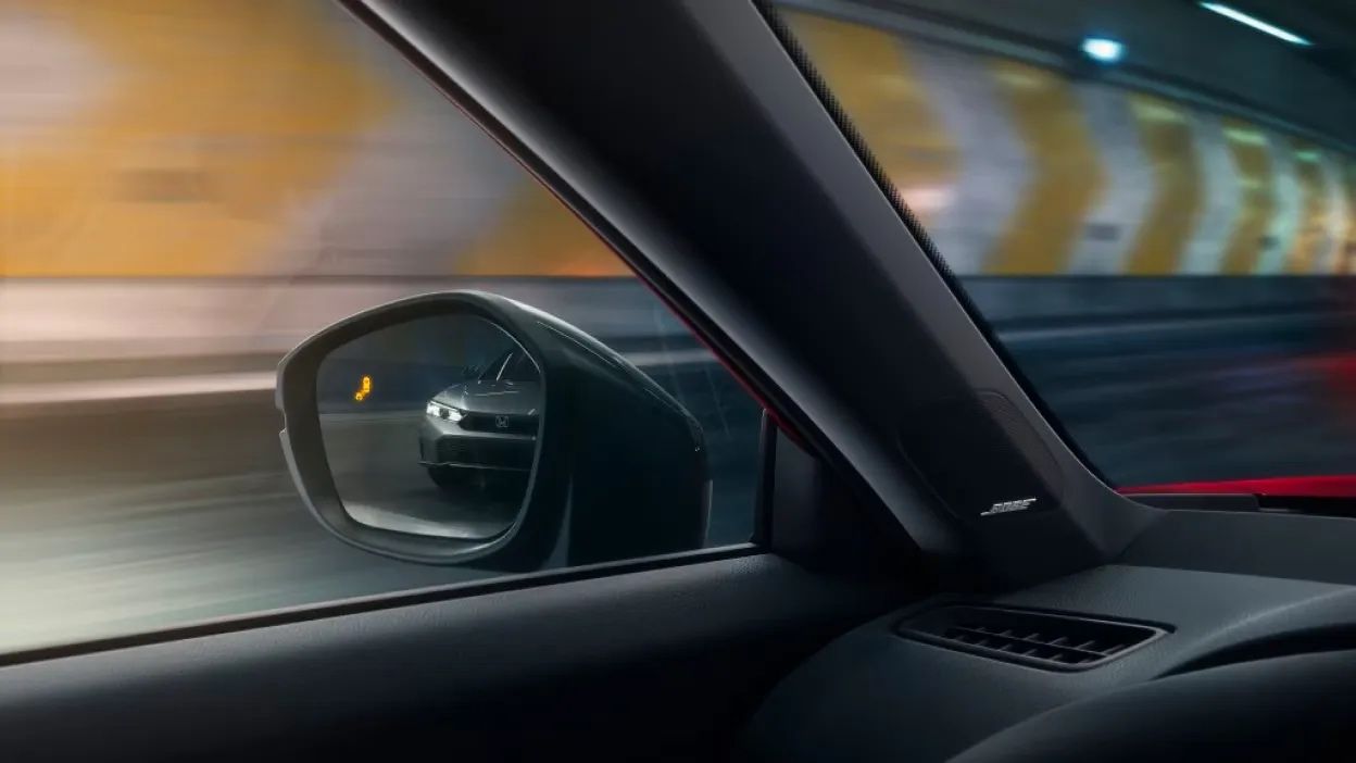 Vue intérieure de la Honda Civic hybride 2026 en conduite dans un tunnel, avec rétroviseur gauche reflétant un véhicule arrière et détails du système audio Bose sur le pilier.