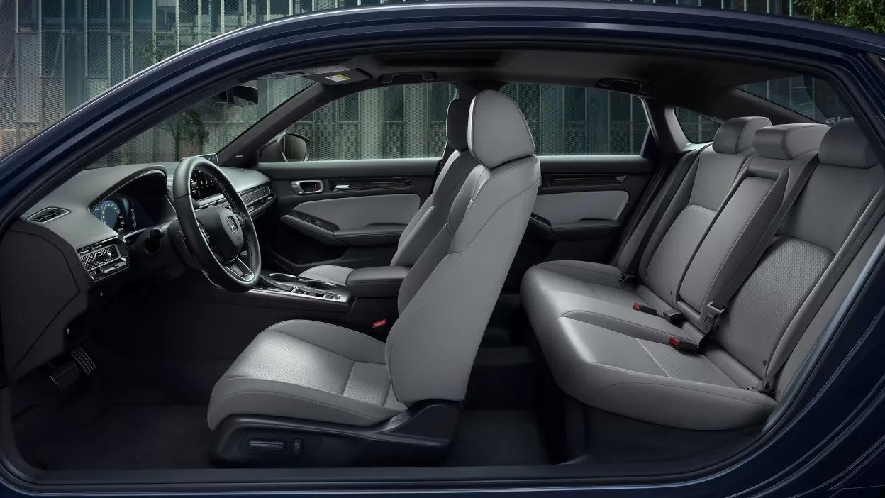 Vue latérale intérieure de l’habitacle de la Honda Civic hybride 2026 avec sièges avant et arrière en tissu gris, volant multifonction et console centrale moderne.