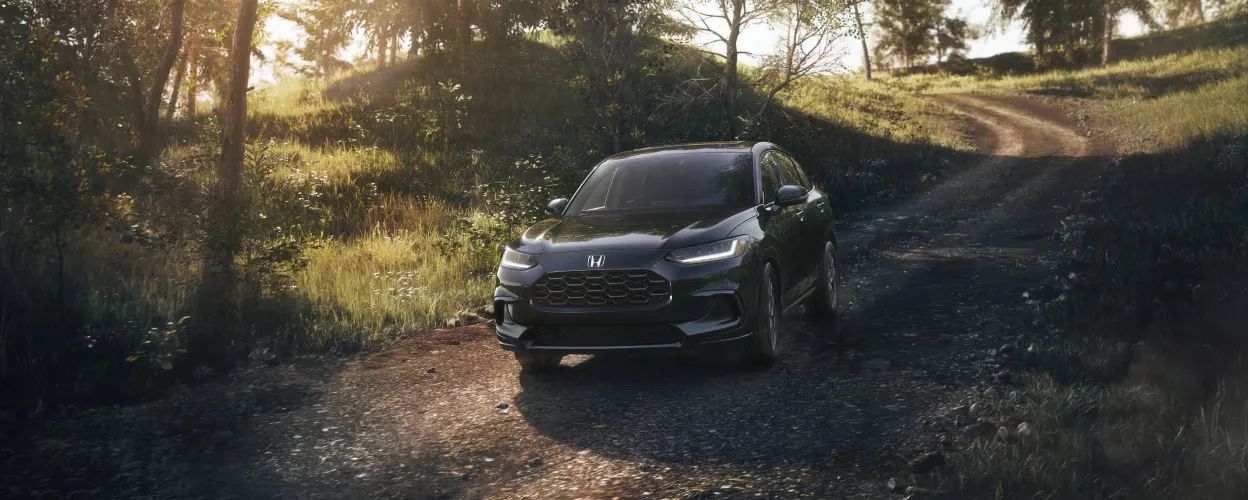 Honda HR-V 2026 noir sur un sentier de gravelle en forêt, éclairé par une lumière dorée de fin de journée.