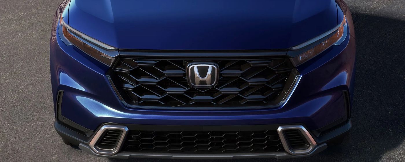 Gros plan sur la calandre noire du Honda CR-V hybride 2026 bleu stationné, soulignant le logo Honda et la finition haut de gamme du modèle.