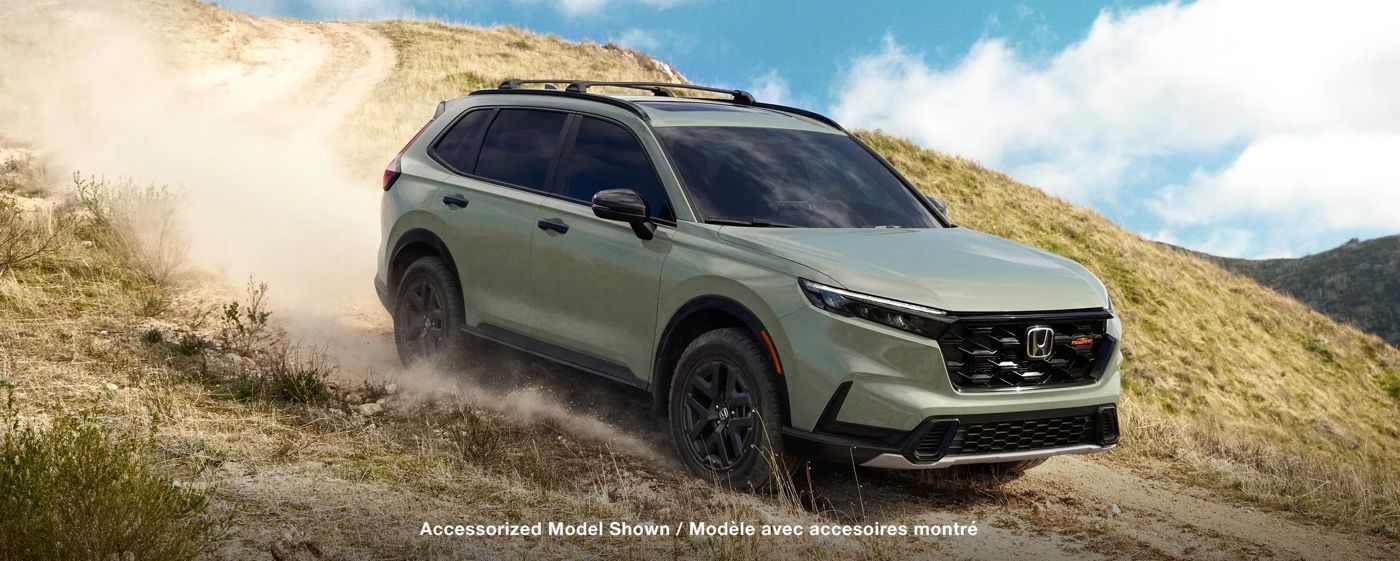 Honda CR-V hybride 2026 TrailSport vert roulant sur un chemin de terre en montagne, démontrant ses capacités hors route et son style robuste.