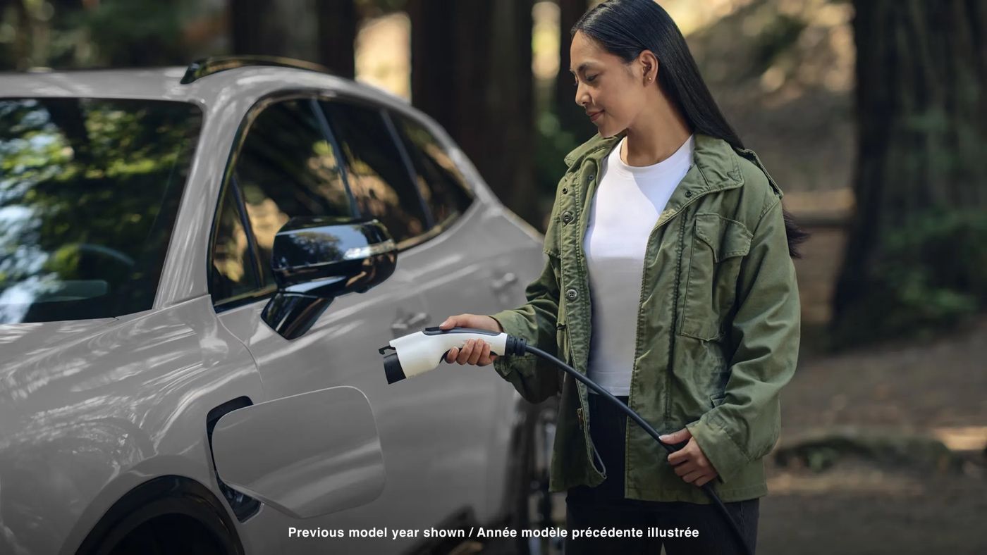 Femme branchant un chargeur sur le Honda Prologue 2025 électrique gris stationné en forêt, mettant en valeur le côté pratique de la recharge à domicile.