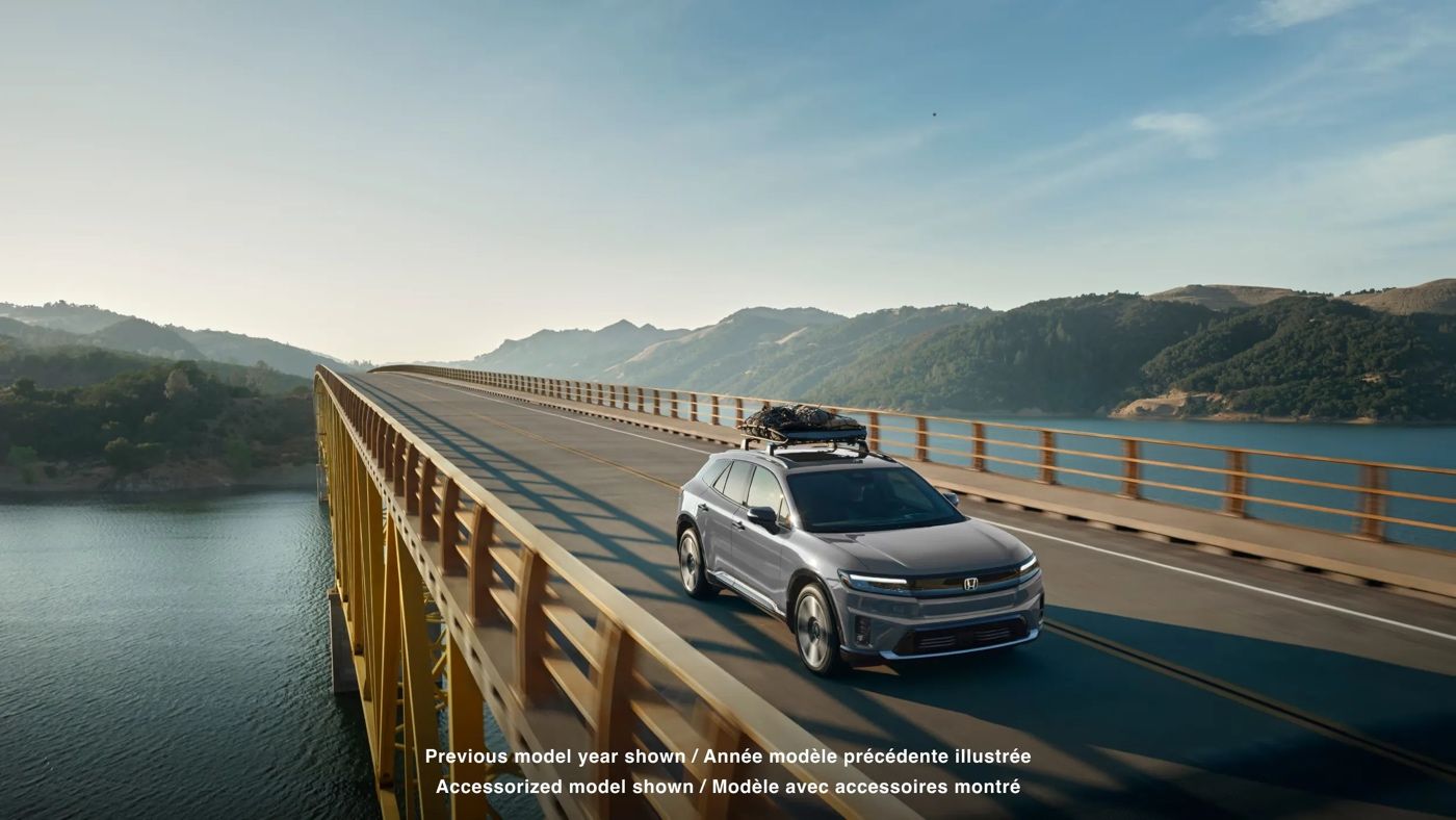 Honda Prologue 2025 électrique gris traversant un pont au-dessus d’un lac, démontrant son autonomie et ses capacités en voyage longue distance.