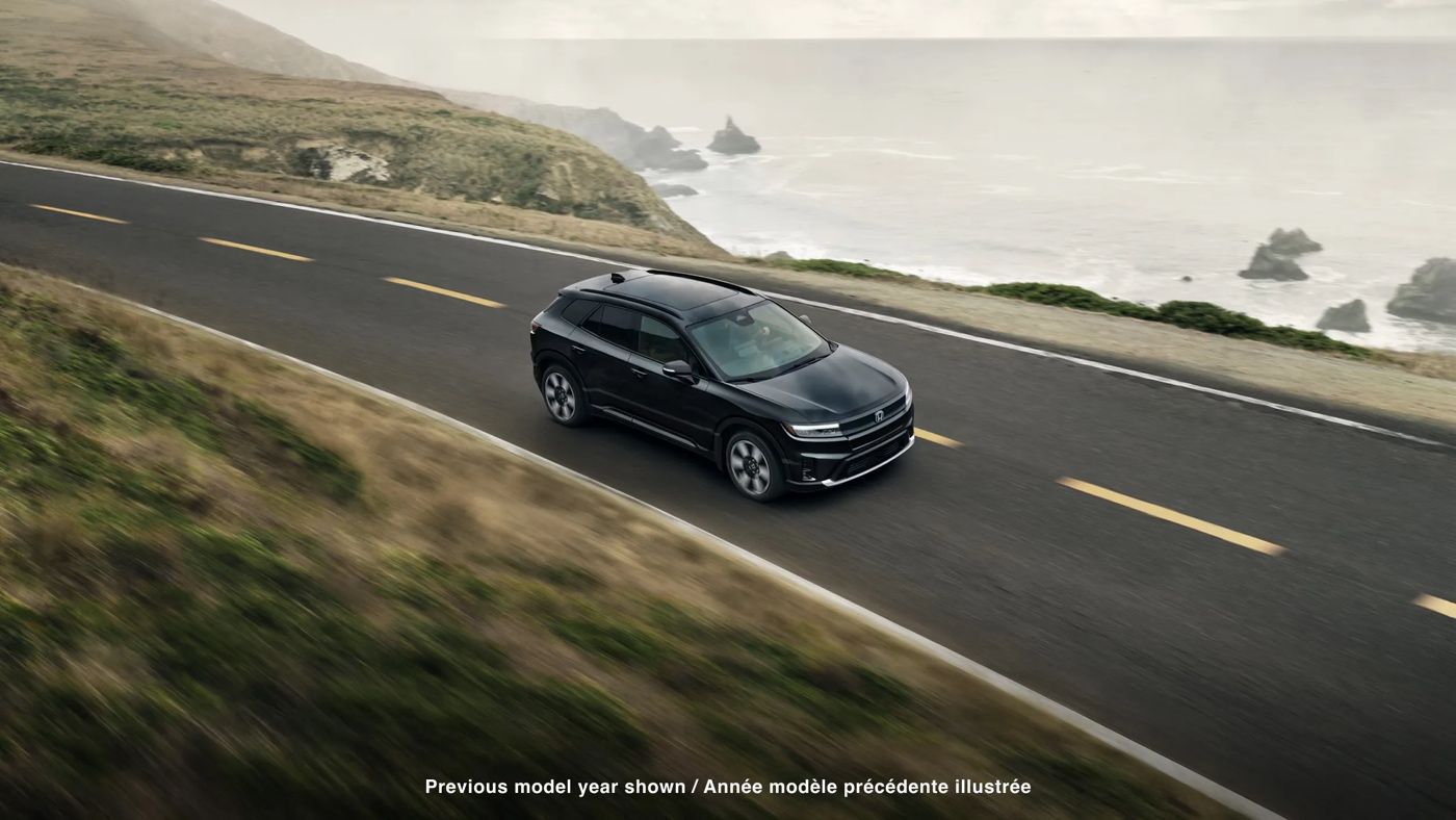 Vue aérienne du Honda Prologue 2025 noir entièrement électrique roulant près du littoral, illustrant sa tenue de route et son côté aventure.