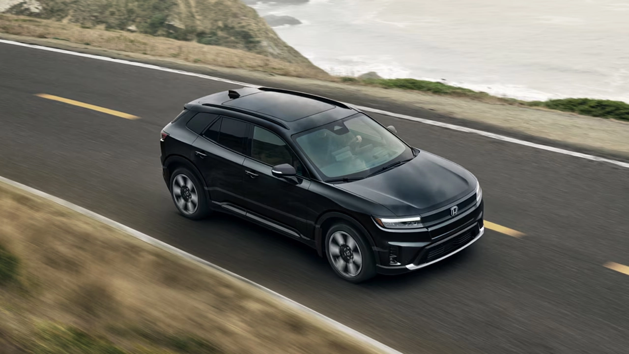 Vue 3/4 avant et lat&eacute;rale du Honda Prologue sur route avec vue sur mer