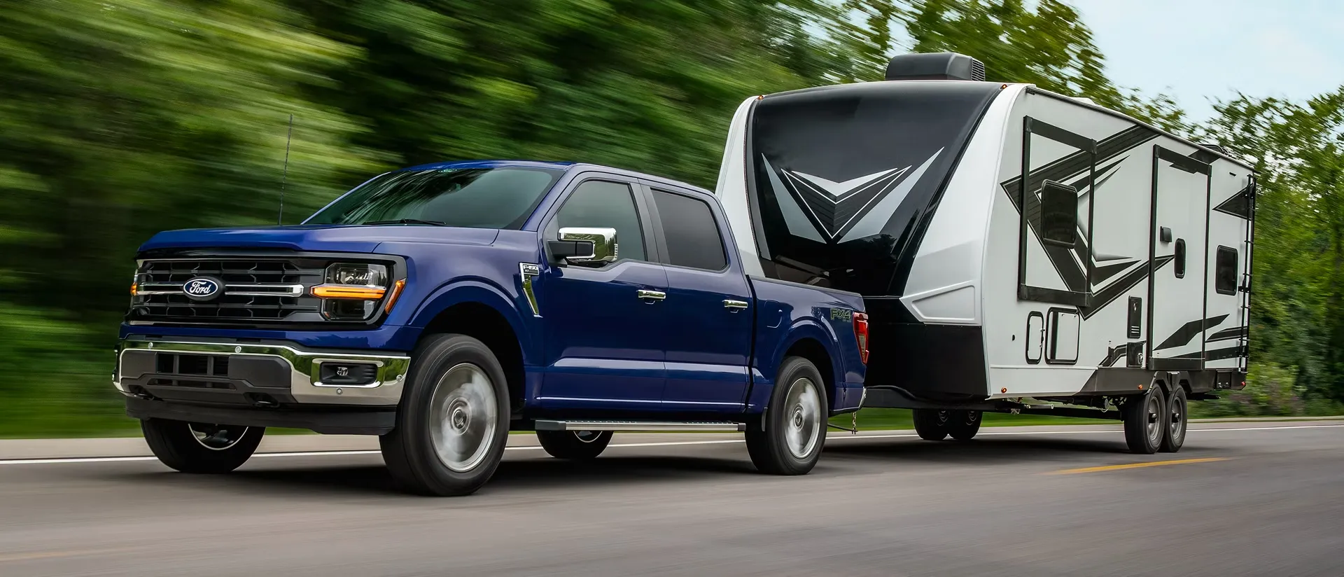 Blue Ford F-150 towing a camper on the road.