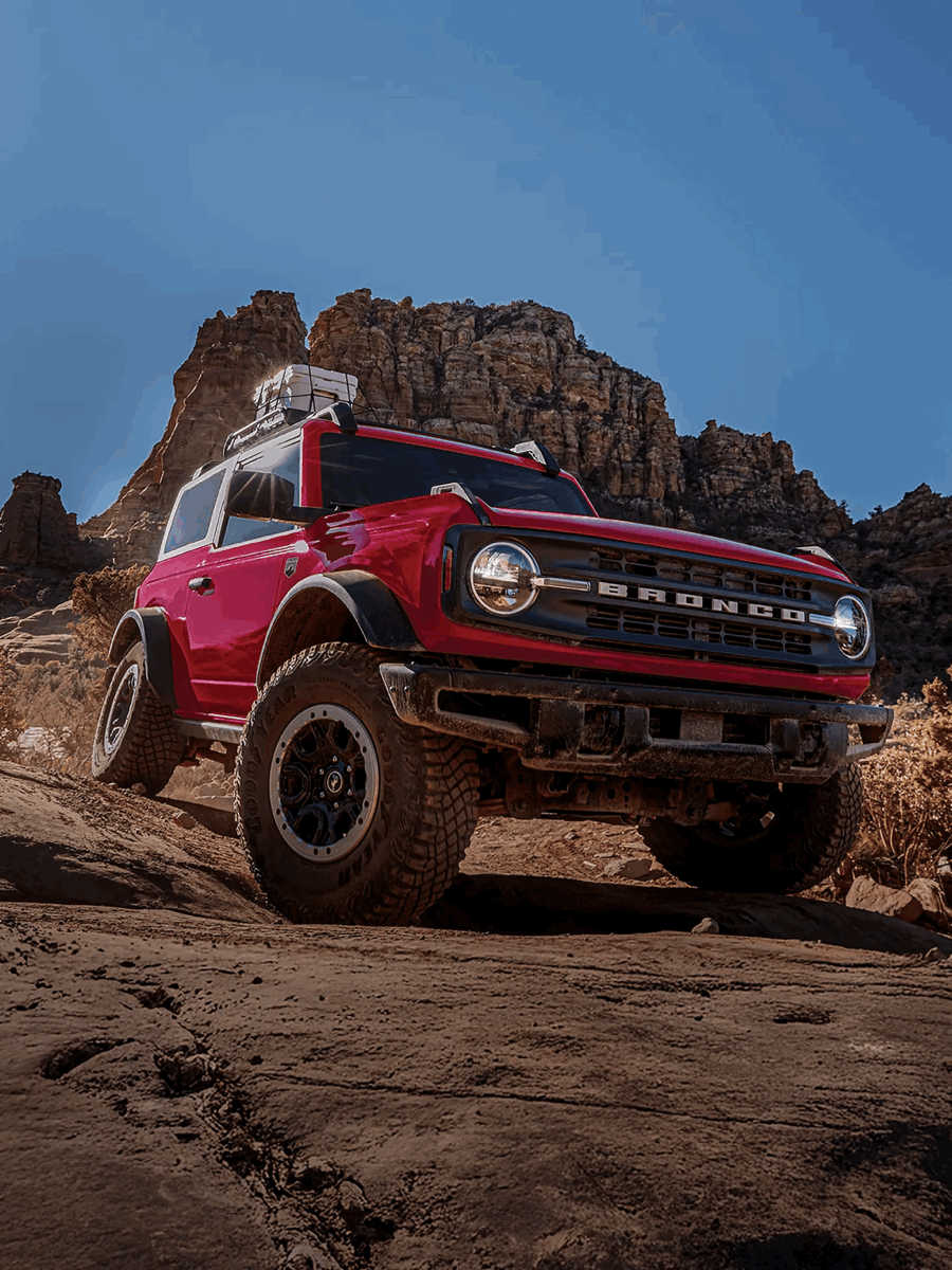 Red Ford Bronco driving on a rocky trail.