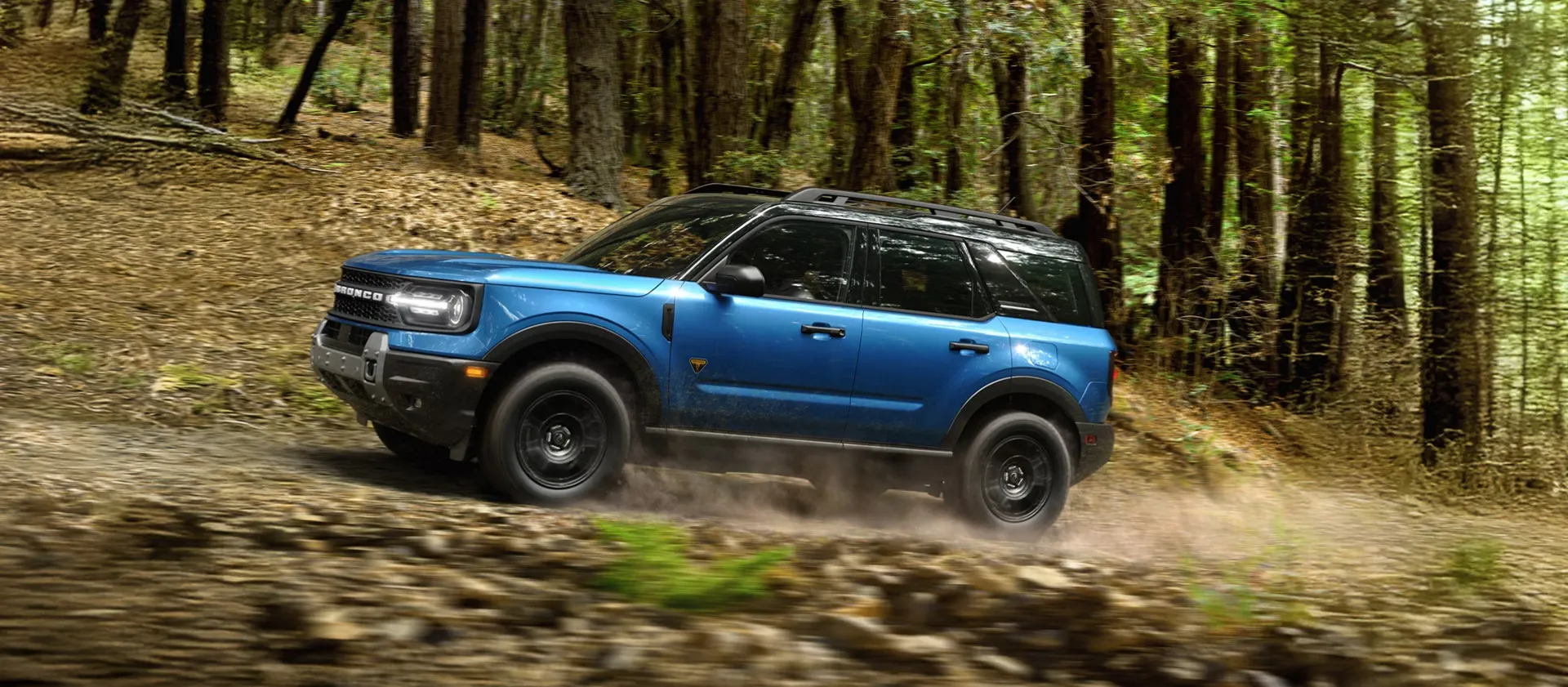 Blue Ford Bronco Sport driving on a forest trail.