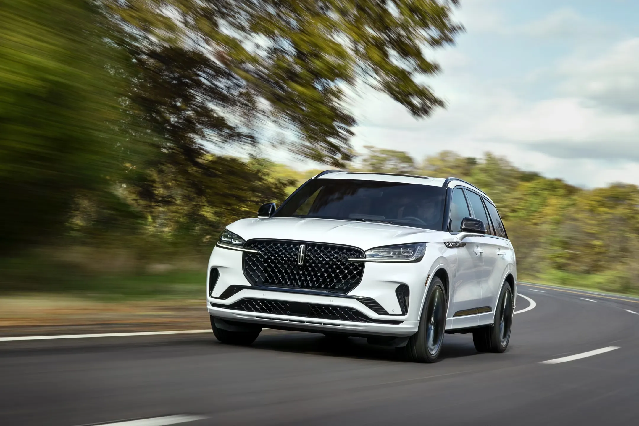 White Lincoln Aviator driving on a tree-lined road.