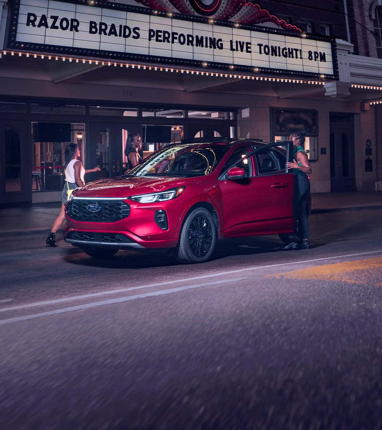 Ford Escape 2026 rouge stationn&eacute; devant un th&eacute;&acirc;tre en soir&eacute;e.