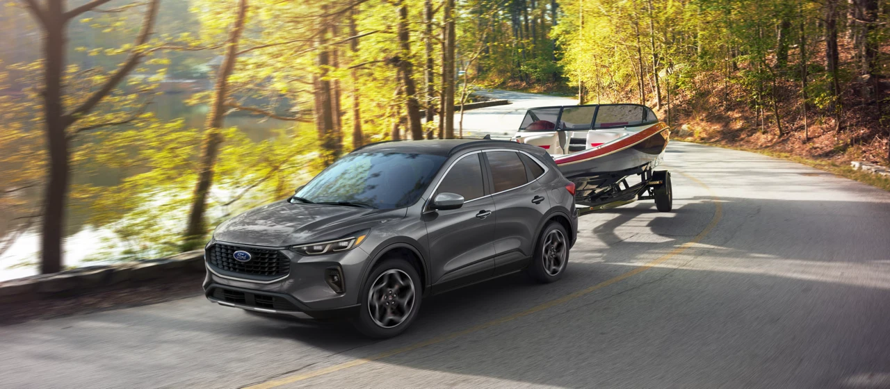 2026 Ford Escape towing a boat on a wooded road.