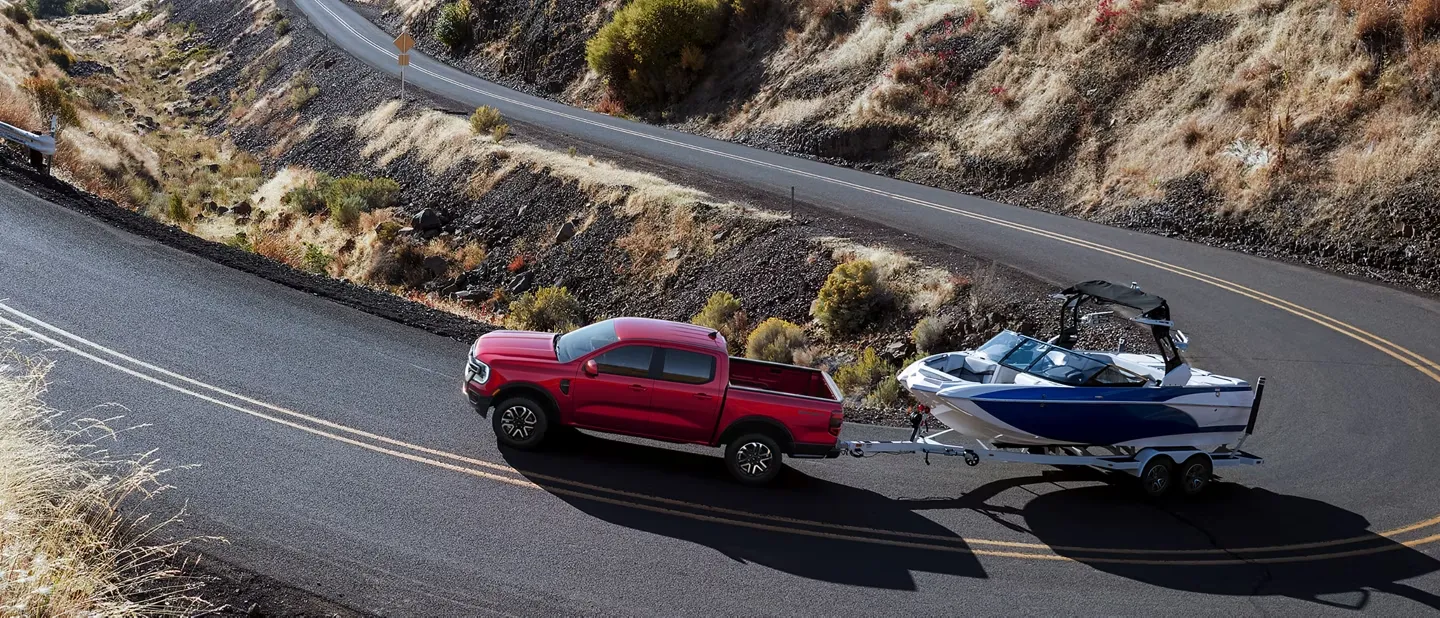 Red 2026 Ford Ranger towing a boat on a mountain road.