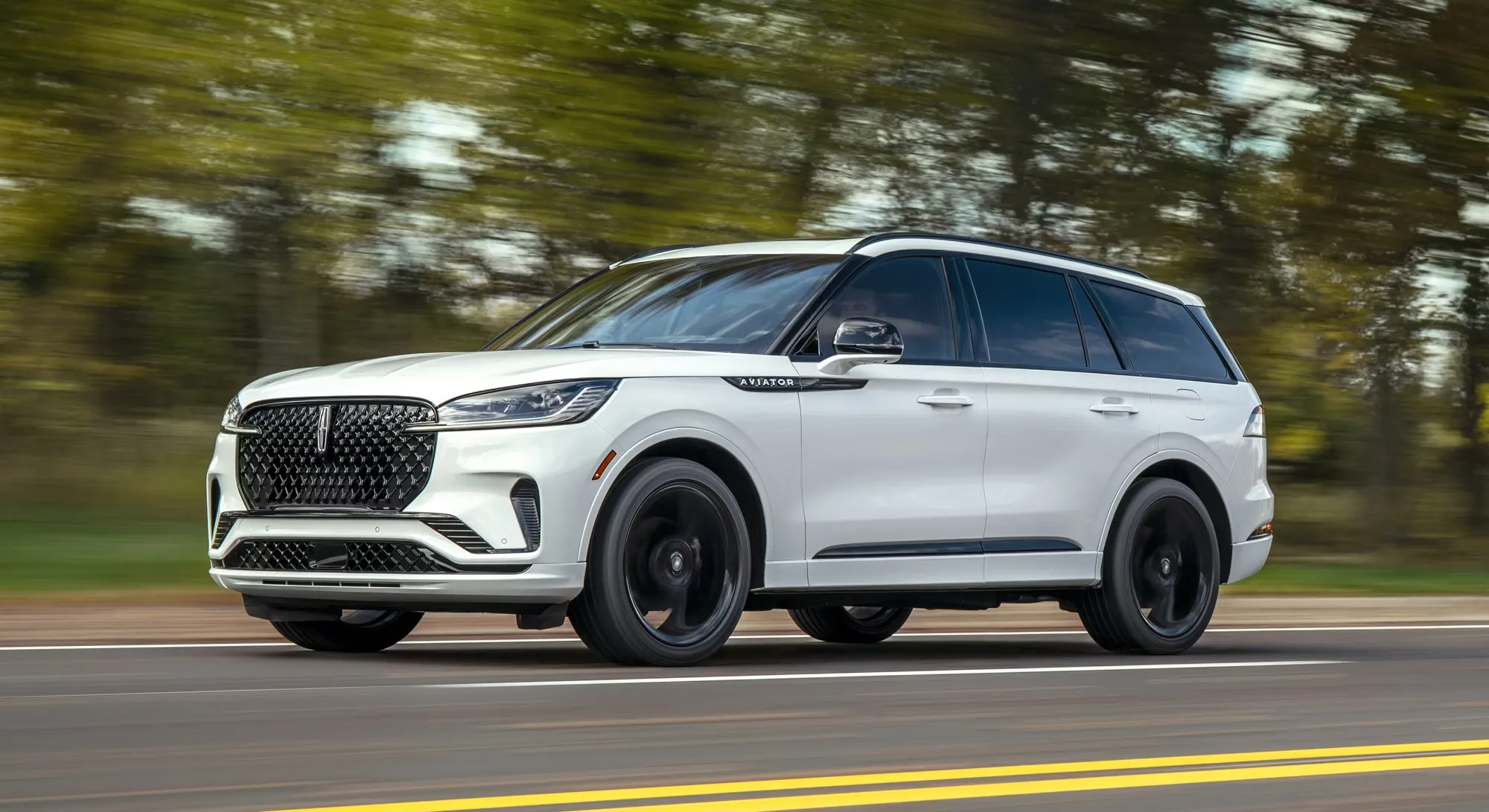 White 2026 Lincoln Aviator driving on a wooded road.