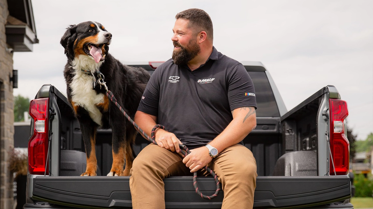 A Paillé employee, sitting on the open tailgate of a Chevrolet Silverado with his dog, because the right vehicle is one that fits your life and the people who matter to you.