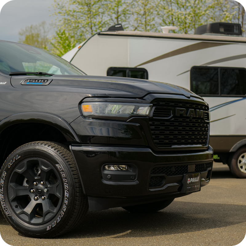 Ram 1500 noir, vue avant, garé devant une caravane blanche.