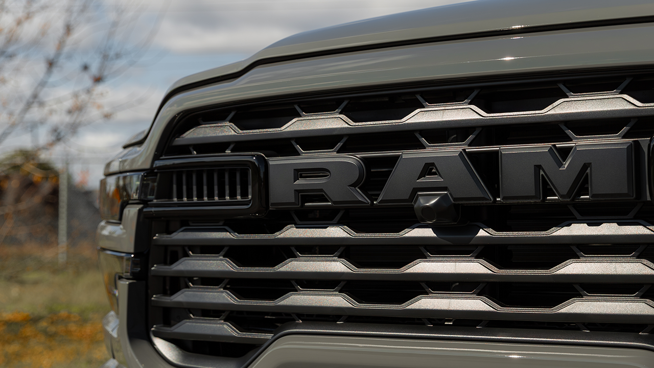Gros plan de la calandre chromée d'un pick-up Ram, avec le logo RAM et un arrière-plan flou d'automne.