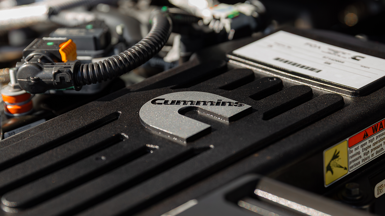 Close-up of the engine cover bearing the Cummins logo, with wiring and a warning label visible in the background.