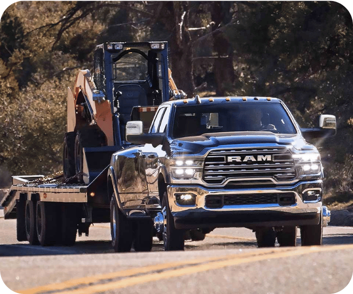 3/4-front view of the 2026 RAM 3500 on the road, towing a heavy tractor