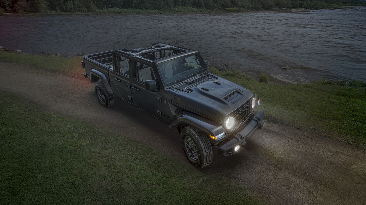 3/4 front and side view of the 2026 Jeep Gladiator on a forest road near a lake in 2026