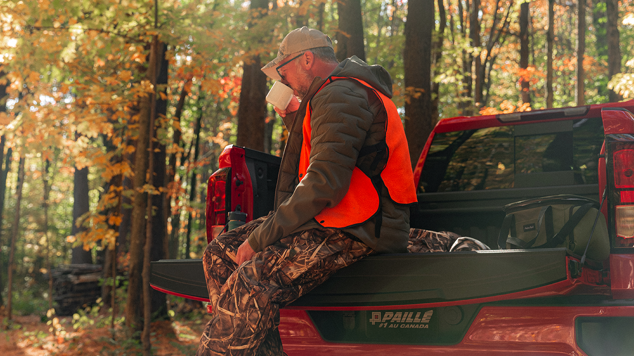 Rear view of the 2027 GMC Sierra and a man drinking his coffee before a hunting trip
