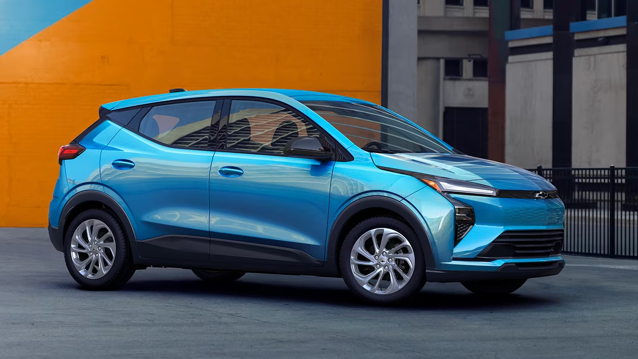 Side view of the 2027 Chevrolet Bolt in a parking lot with its headlights on