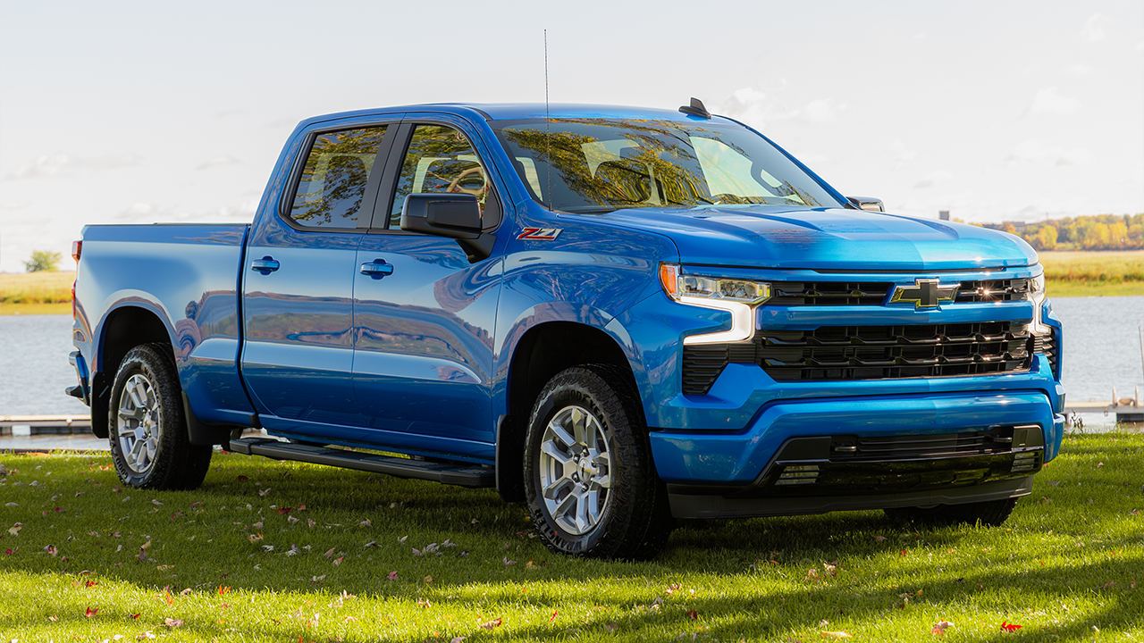Rear view of the standard truck bed on a blue 2026 Silverado 1500 parked in front of a lake