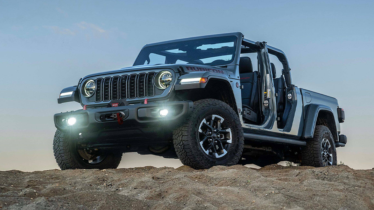3/4 front and side view of a 2026 Jeep Gladiator on a sandy hill with its headlights on