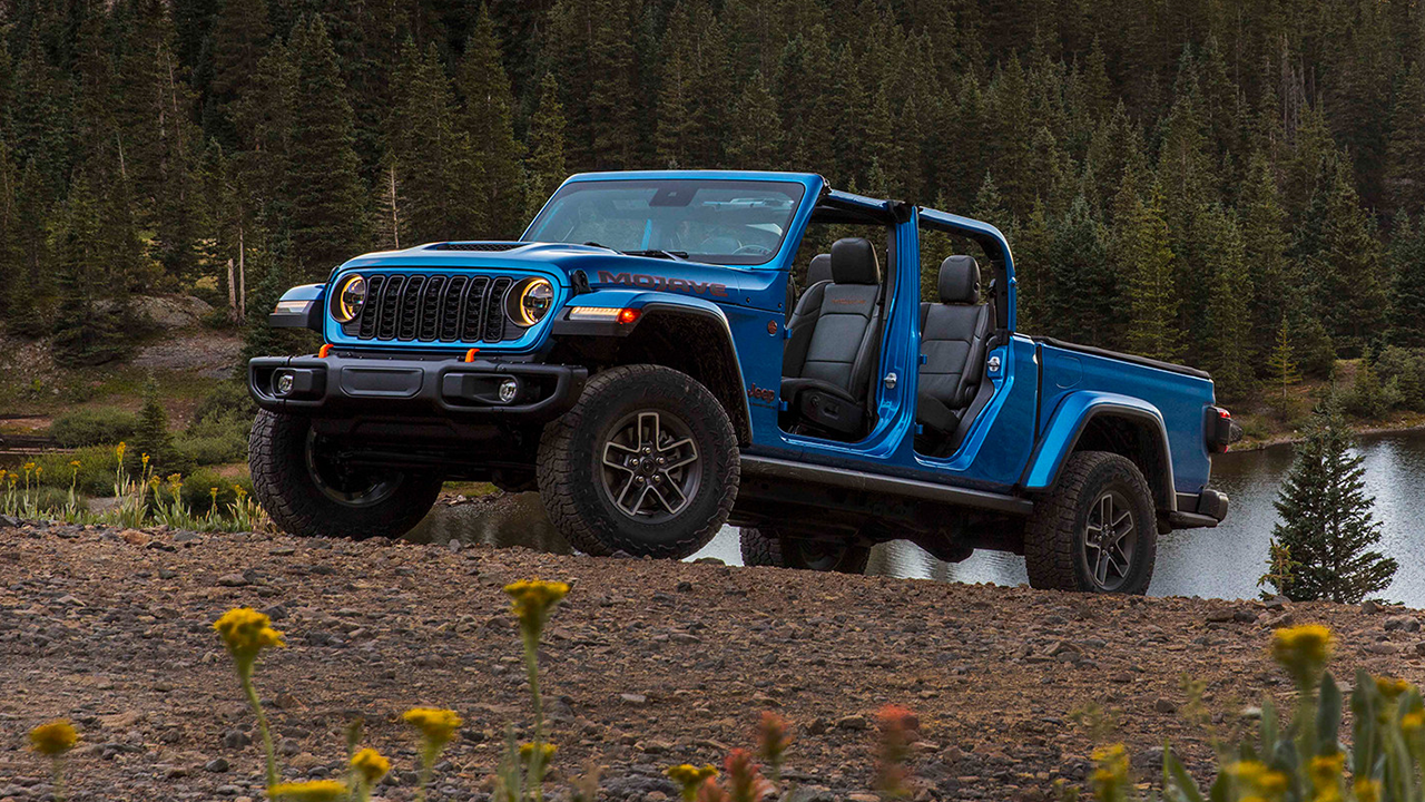3/4 front and side view of a 2026 Jeep Gladiator on a mountain road with a view of a lake in the background