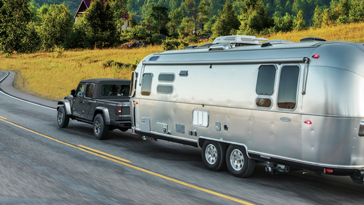 Rear view of the 2026 Jeep Gladiator on the road, towing a trailer.