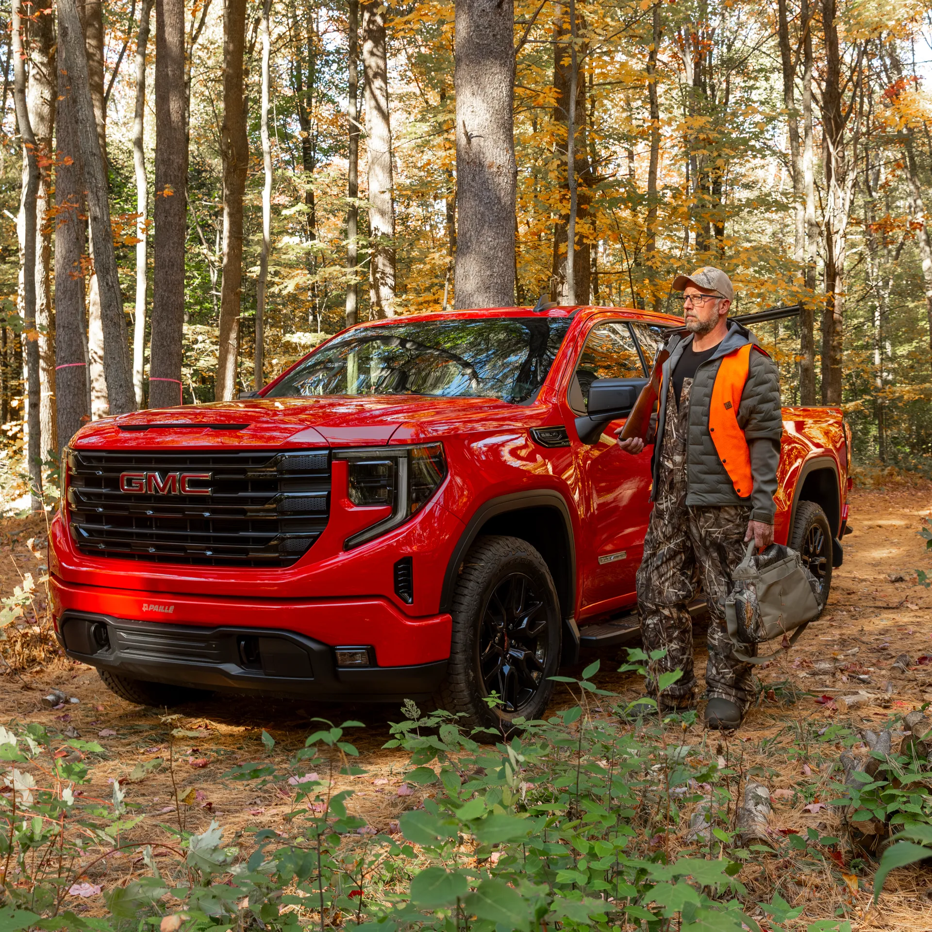 Hunter standing next to his red GMC truck in the forest.