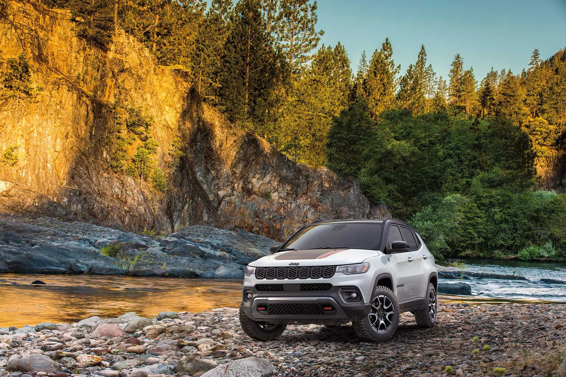 2027 Jeep Compass crossing a rocky trail near a stream.