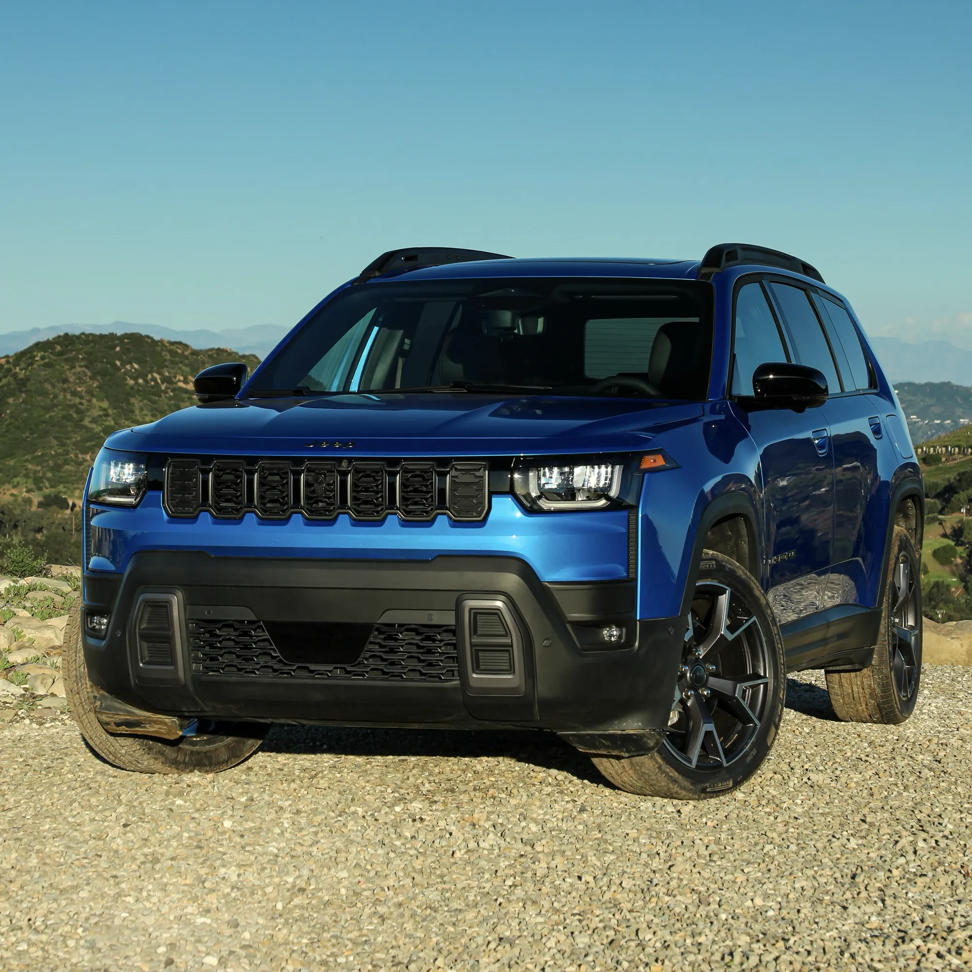Blue Jeep Cherokee hybrid seen from the front on a gravel road.