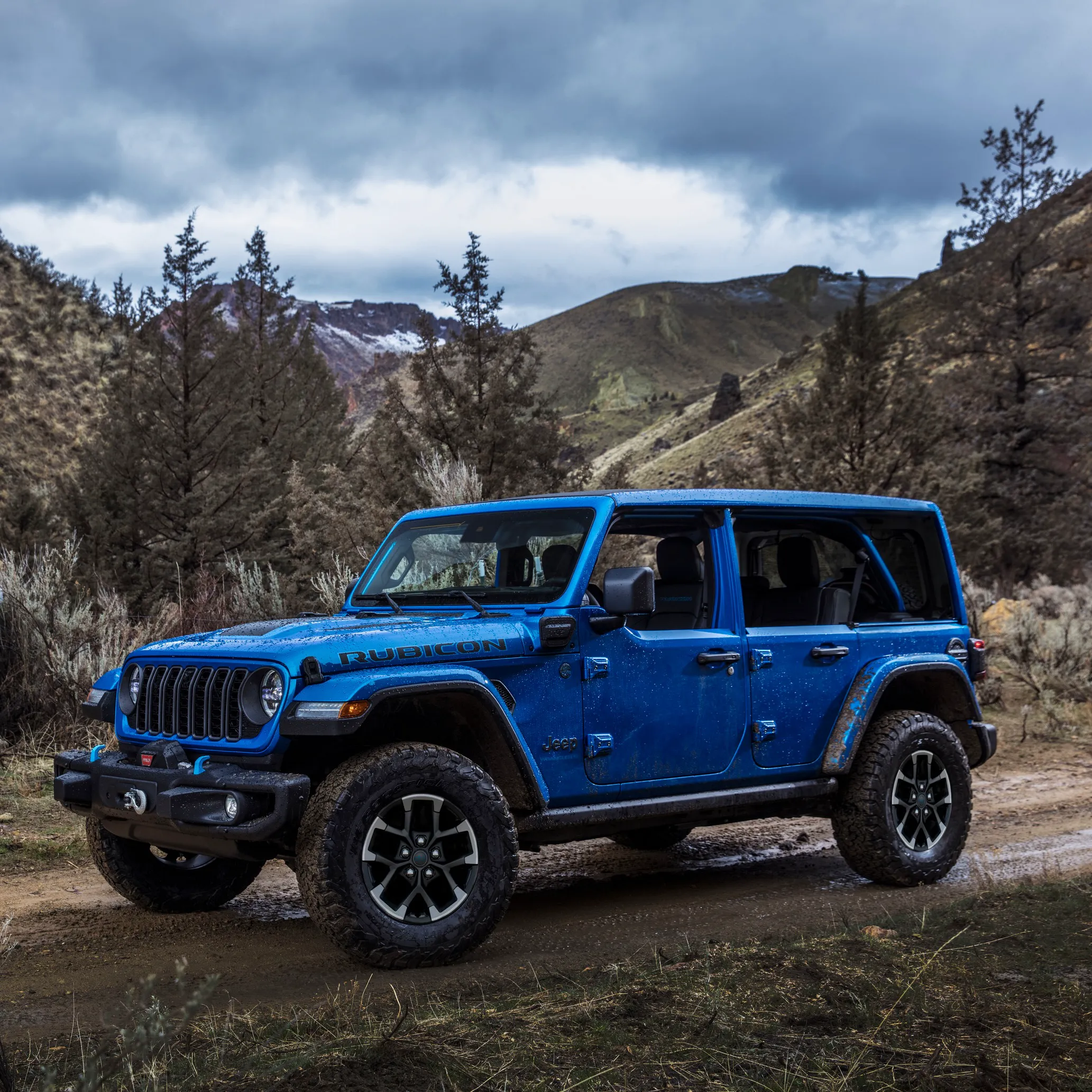 Blue Jeep Wrangler 4xe on rocky terrain with mountains in the background.