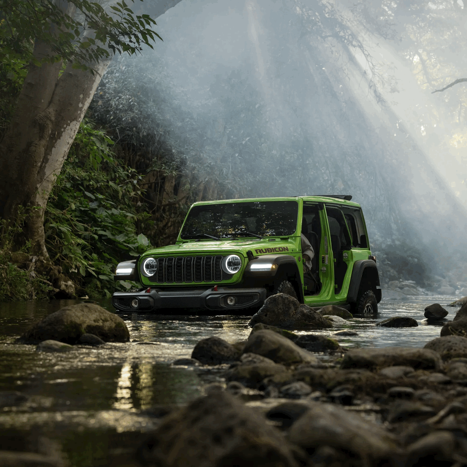 Green Jeep Wrangler crossing a rocky stream in a sunlit forest.