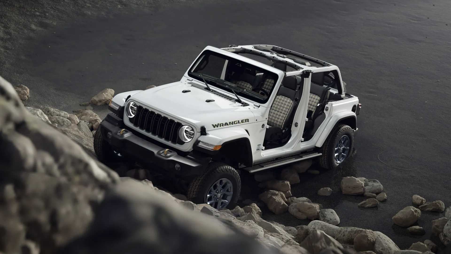 White Jeep Wrangler with no doors or top on rocky terrain by the water.