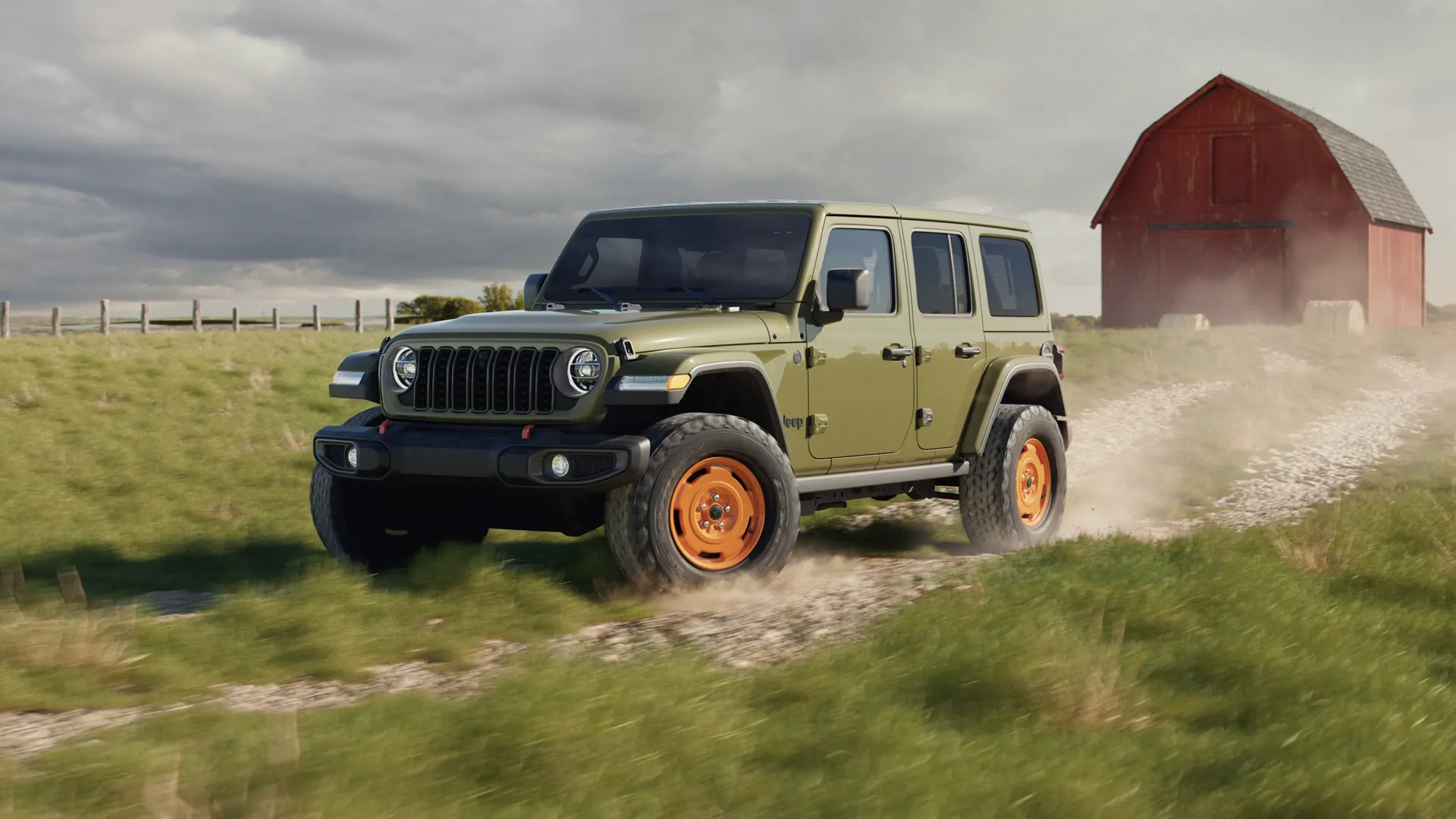 Olive green 4-door Jeep Wrangler with orange wheels on a dirt road in front of a red barn.