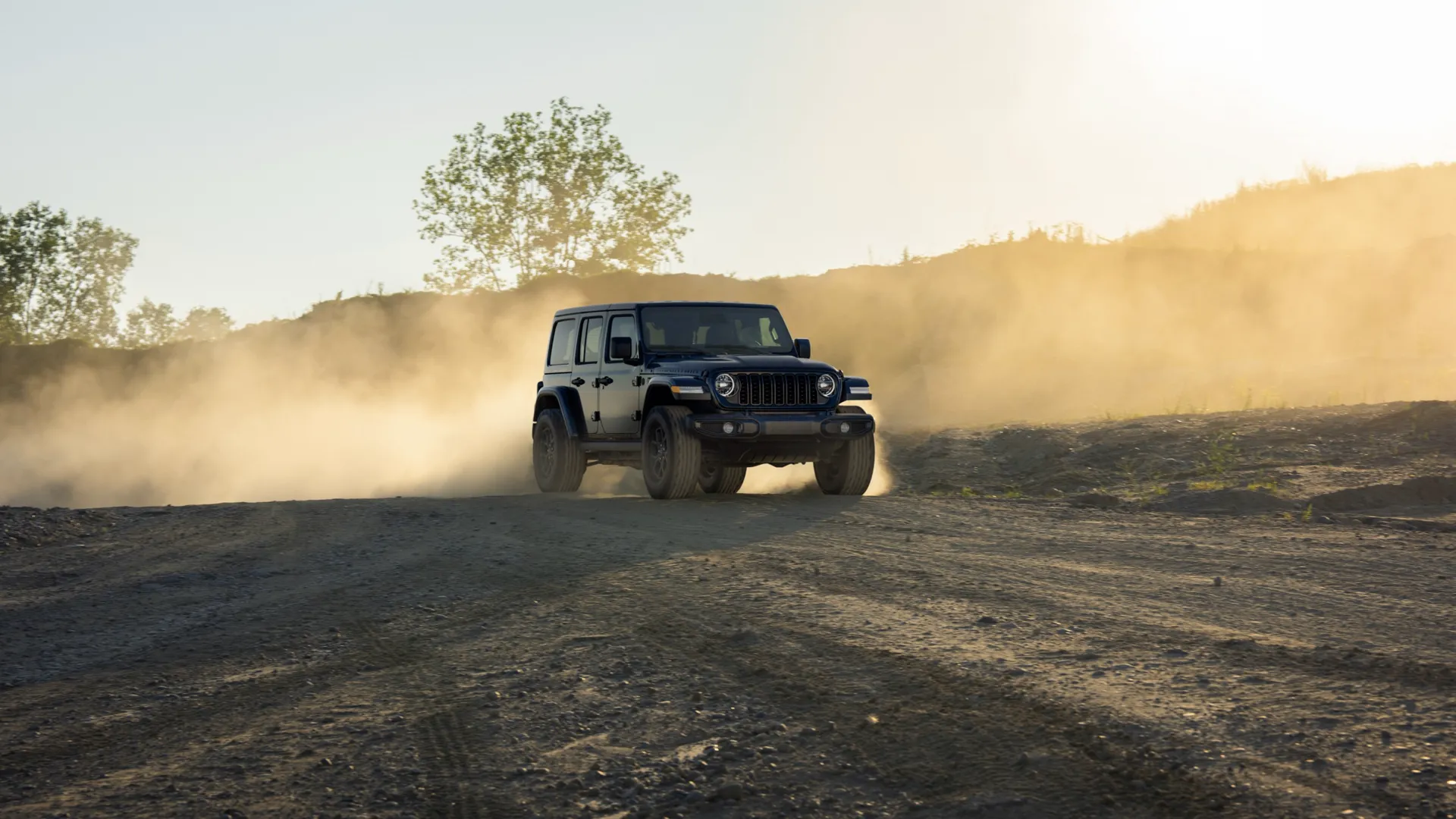 Black Jeep Wrangler kicking up a cloud of dust on a dirt road at sunset.