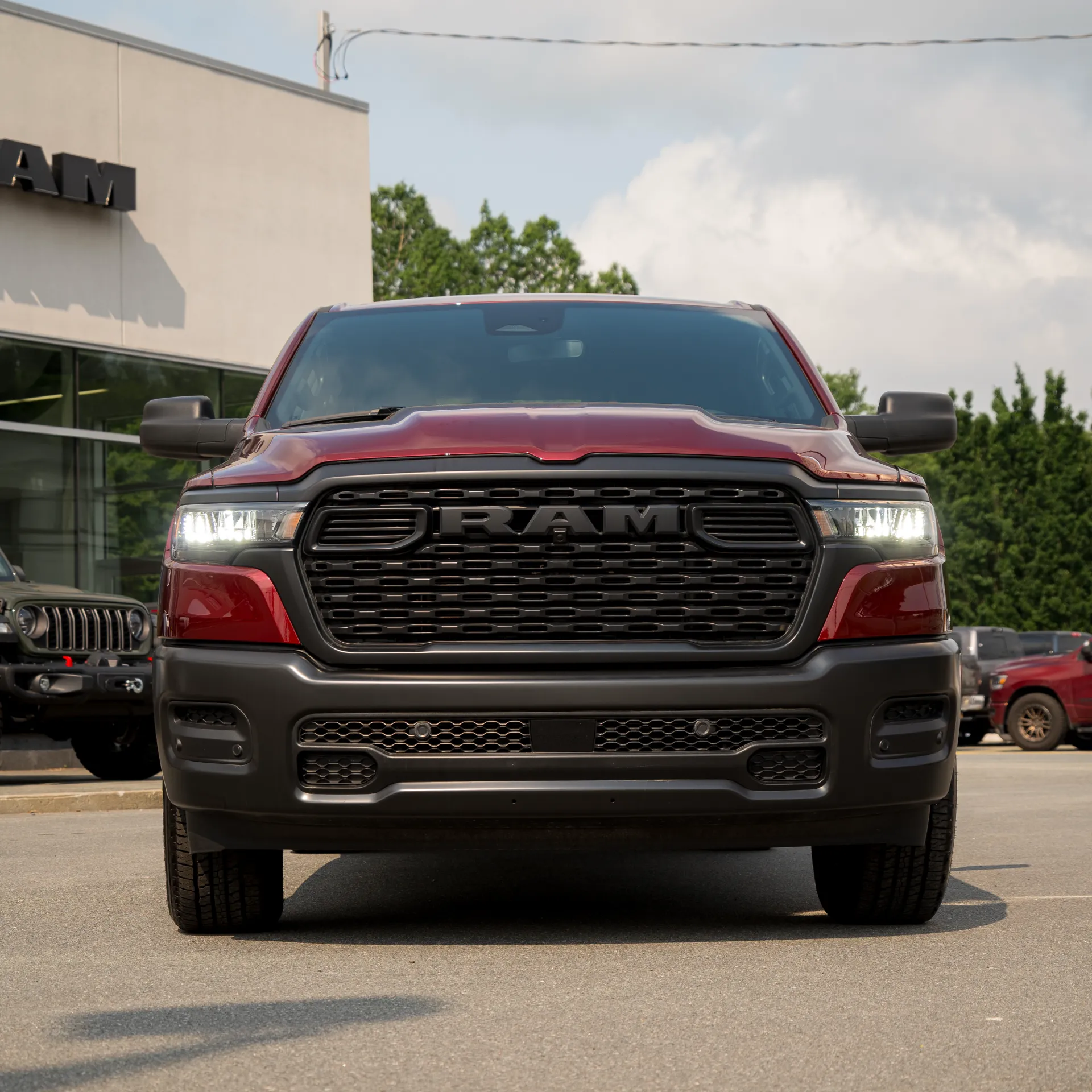 Dark red RAM 1500 seen from the front, parked in front of a RAM dealership.