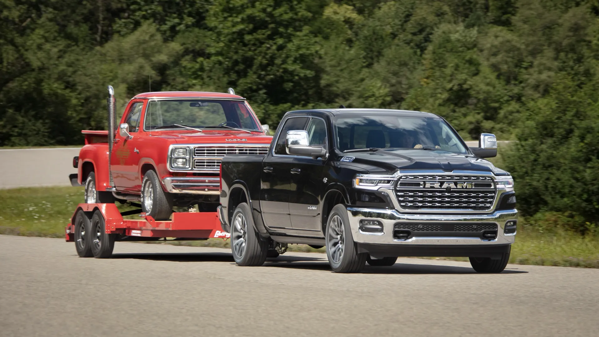 Black RAM 1500 Limited towing a red truck loaded on a trailer, on a tree-lined road.