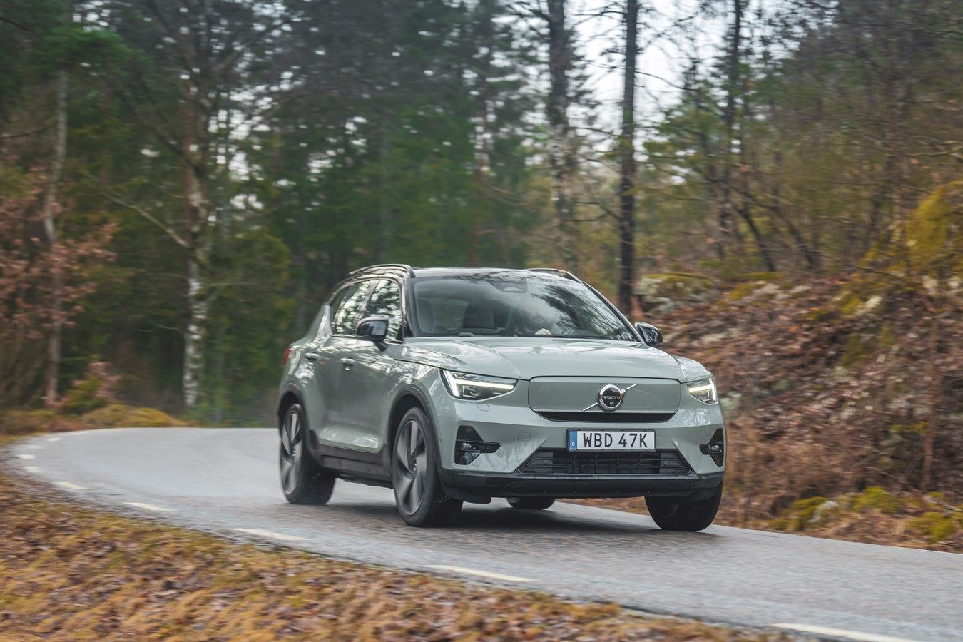 Grey 2026 Volvo EX40 electric SUV driving on a forest road