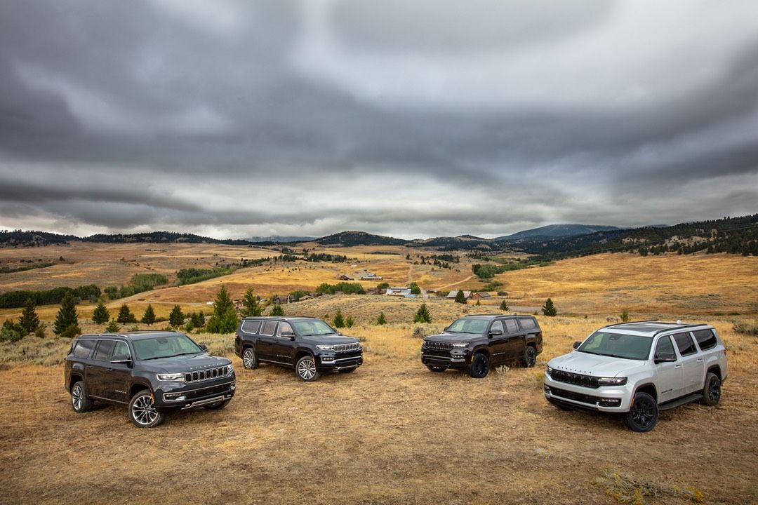 Four 2023 Wagoneer trucks parked on a piece of land in a wilderness area.