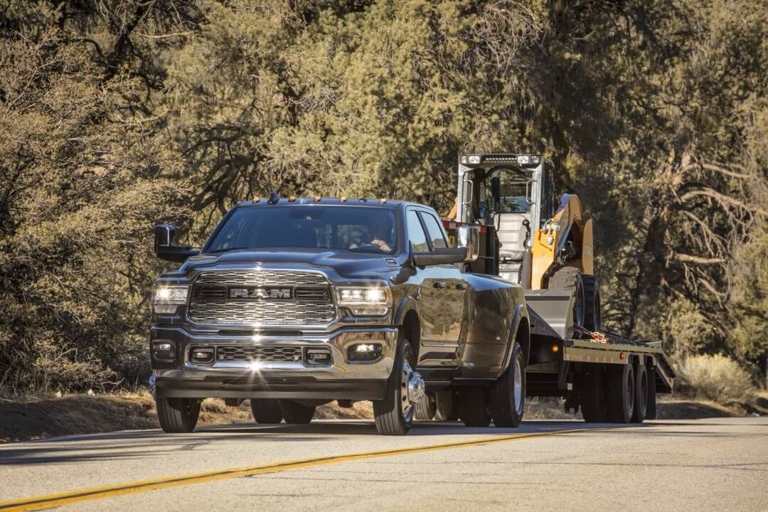 3/4 front view of the 2024 RAM 3500 HD Limited towing a work utility vehicle.