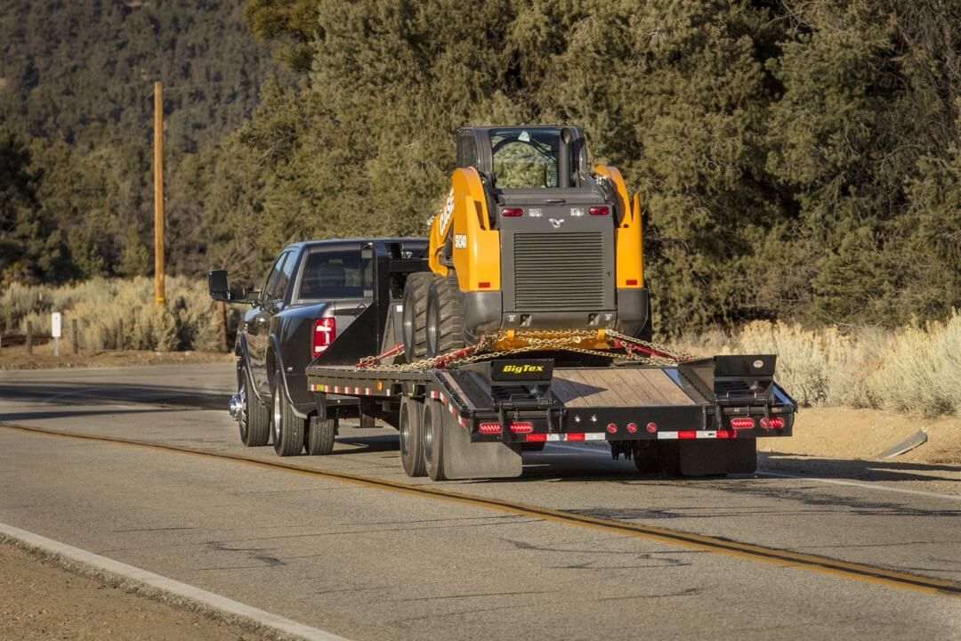 3/4 rear view of the 2024 RAM 3500 HD Limited towing a work utility vehicle.