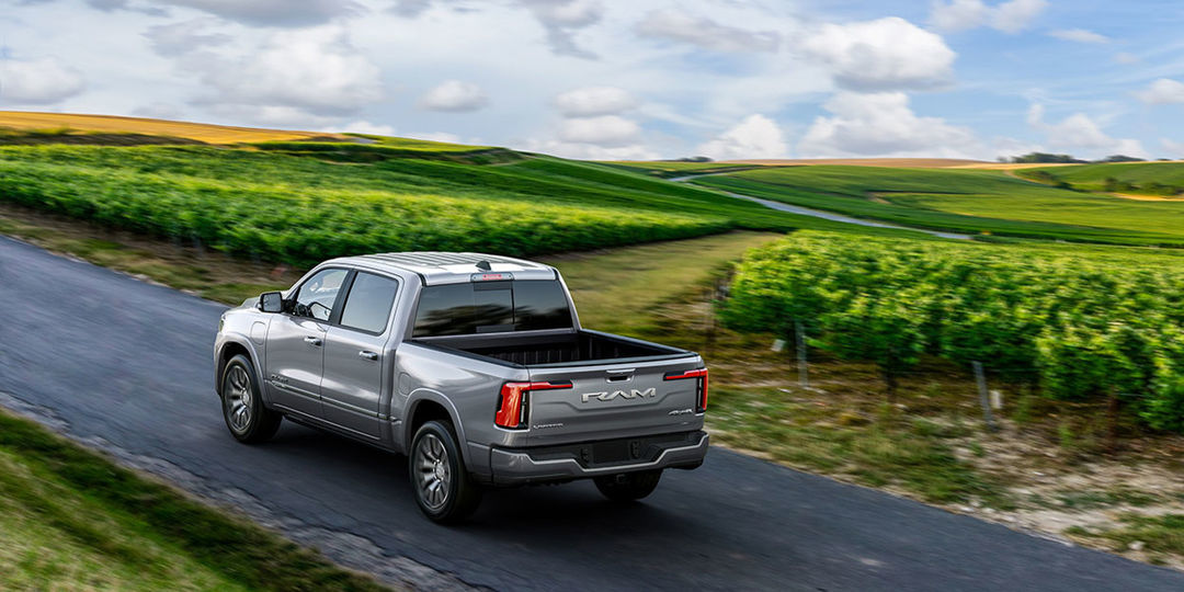 Vue de profil d'un Ram 1500 Ramcharger REx 2025 gris garé sur une colline avec des champs verts au loin.