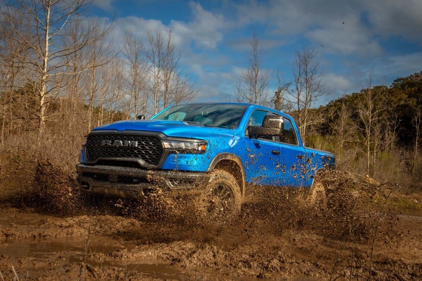 Front 3/4 view of the 2025 RAM 1500 driving through the mud.